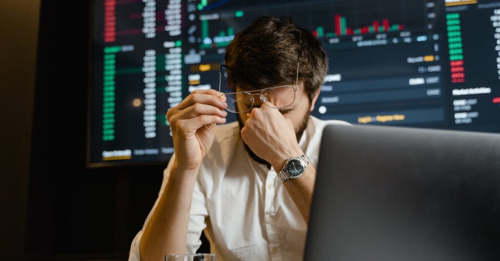 A stressed man looks at stock market data on his computer screen in an office setting.